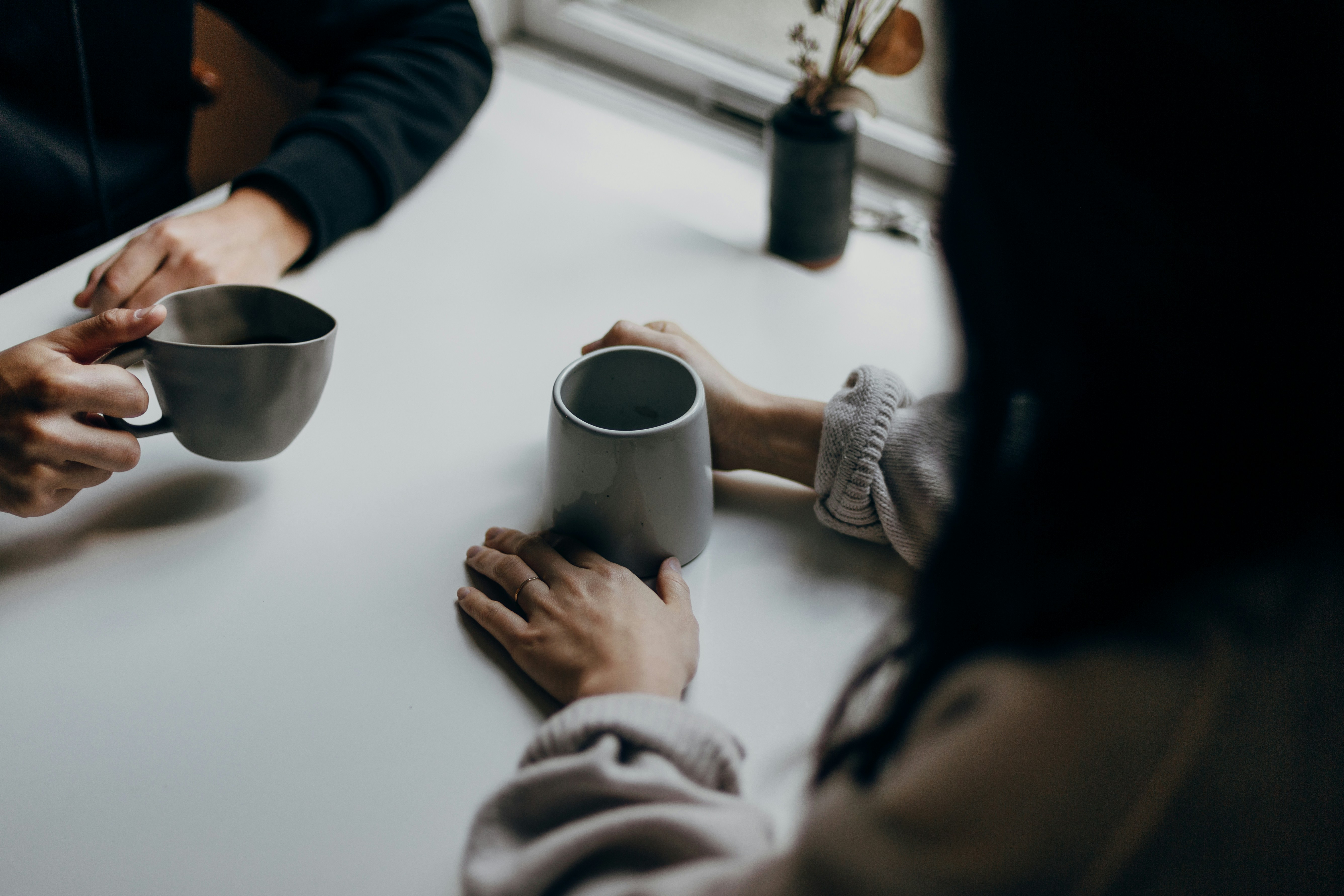 Twee mensen zitten met een mok koffie tegenover elkaar aan tafel