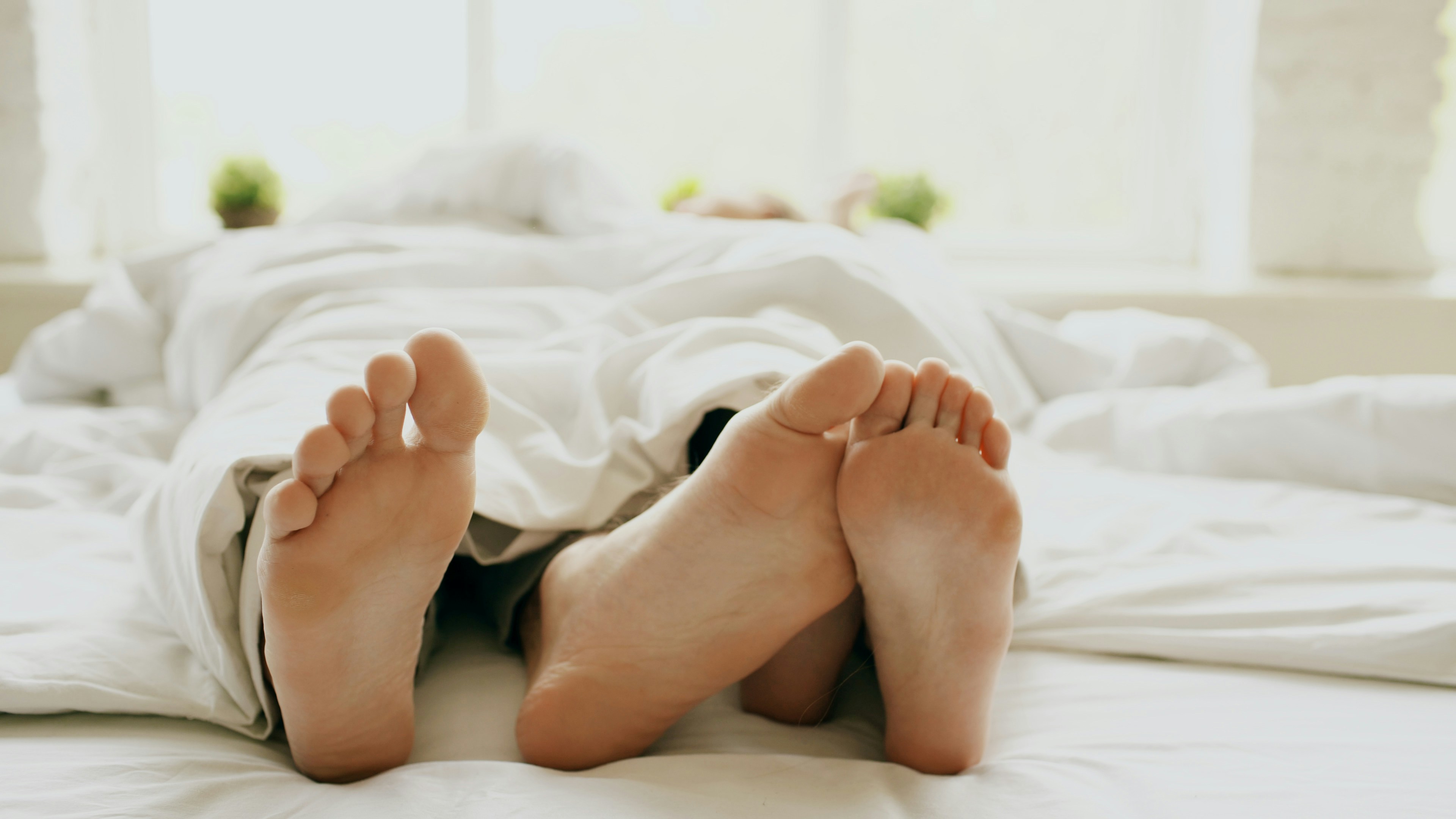 Voeten van twee mensen steken onder een wit dekbed uit